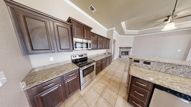 kitchen with visible vents, a tray ceiling, ornamental molding, a stone fireplace, and stainless steel appliances