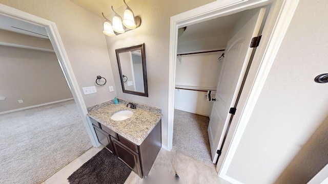 bathroom featuring vanity, a walk in closet, a notable chandelier, and baseboards