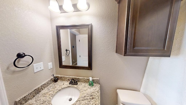 half bath featuring vanity, toilet, and a textured wall