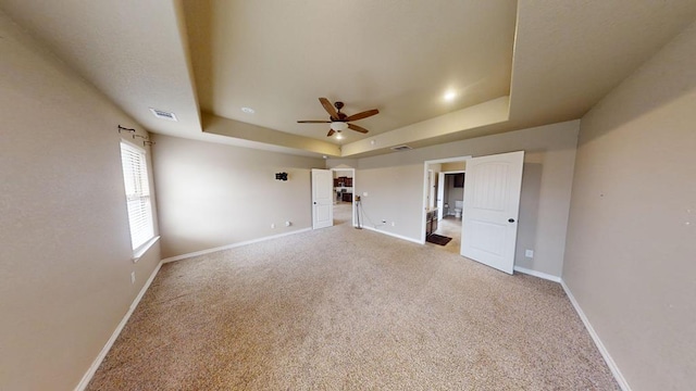 unfurnished bedroom with a ceiling fan, carpet, baseboards, visible vents, and a tray ceiling