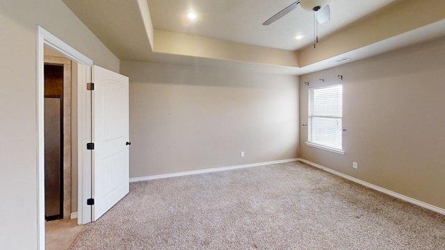 unfurnished room featuring light colored carpet, a ceiling fan, a tray ceiling, and baseboards