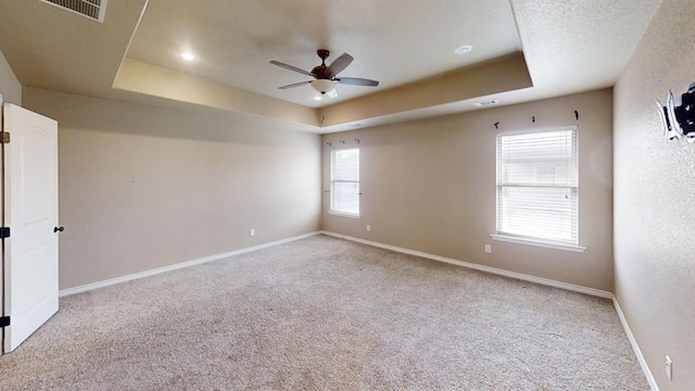 carpeted empty room with baseboards, visible vents, a tray ceiling, ceiling fan, and a textured ceiling