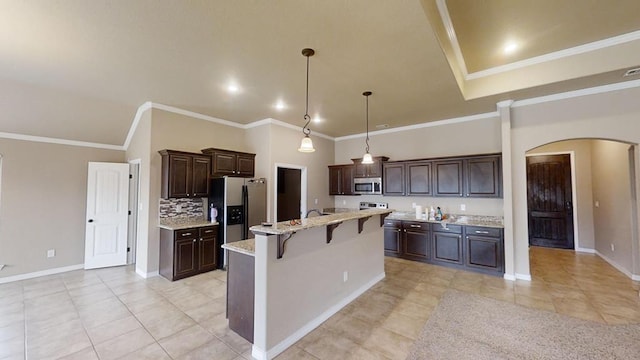 kitchen with dark brown cabinets, a center island with sink, a kitchen breakfast bar, arched walkways, and stainless steel appliances