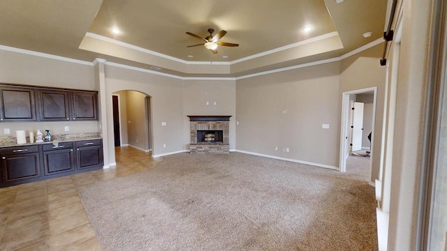 unfurnished living room with a raised ceiling, arched walkways, a fireplace, baseboards, and ceiling fan