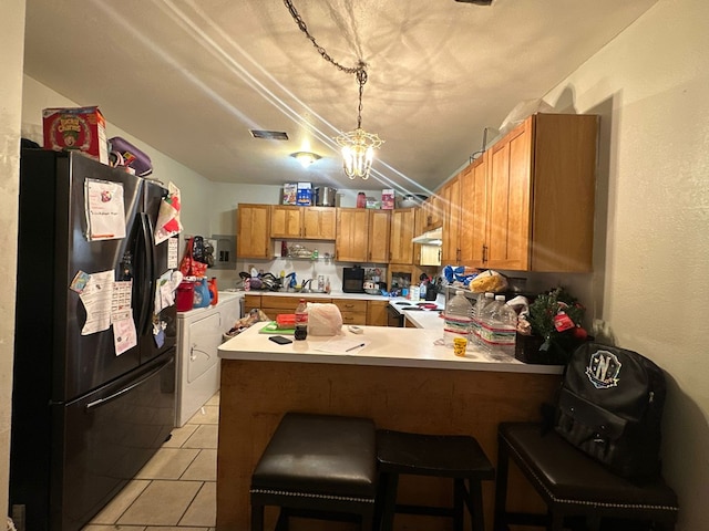 kitchen with black refrigerator, light tile patterned floors, a breakfast bar, and kitchen peninsula