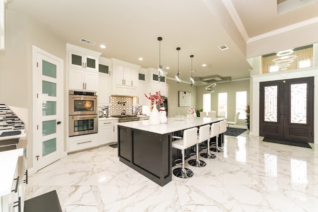 kitchen featuring a breakfast bar area, a center island with sink, white cabinets, decorative light fixtures, and backsplash