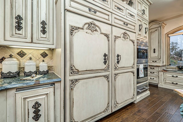 kitchen with stainless steel double oven, tasteful backsplash, dark hardwood / wood-style floors, cream cabinetry, and ornamental molding