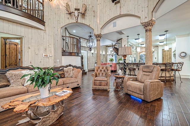 living room with wooden walls, dark hardwood / wood-style floors, a high ceiling, and decorative columns