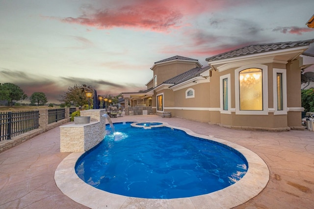 pool at dusk featuring pool water feature, an in ground hot tub, and a patio