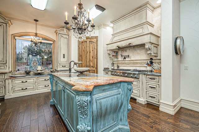 kitchen featuring pendant lighting, stainless steel gas cooktop, a kitchen island with sink, and dark stone countertops