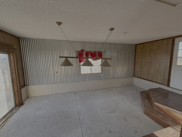 unfurnished dining area with concrete floors, a textured ceiling, and wooden walls