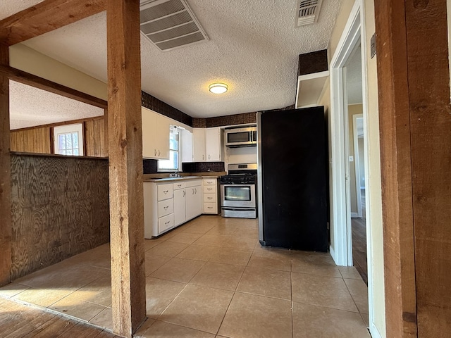 kitchen featuring wooden walls, appliances with stainless steel finishes, light tile patterned flooring, white cabinets, and sink