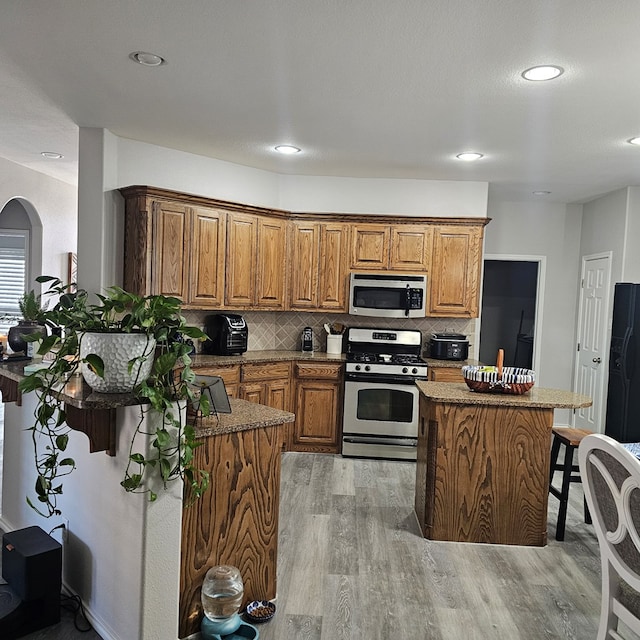 kitchen featuring stainless steel appliances, a kitchen island, backsplash, and light wood-type flooring