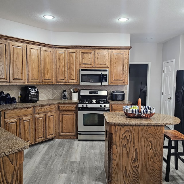 kitchen with a kitchen bar, a kitchen island, stainless steel appliances, light hardwood / wood-style floors, and decorative backsplash