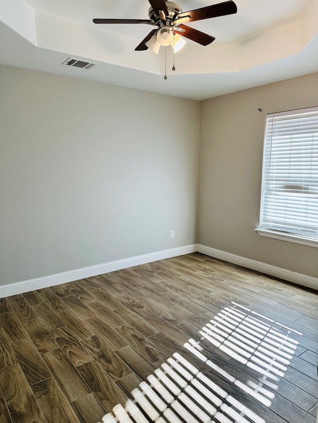 empty room featuring a raised ceiling, ceiling fan, and hardwood / wood-style flooring