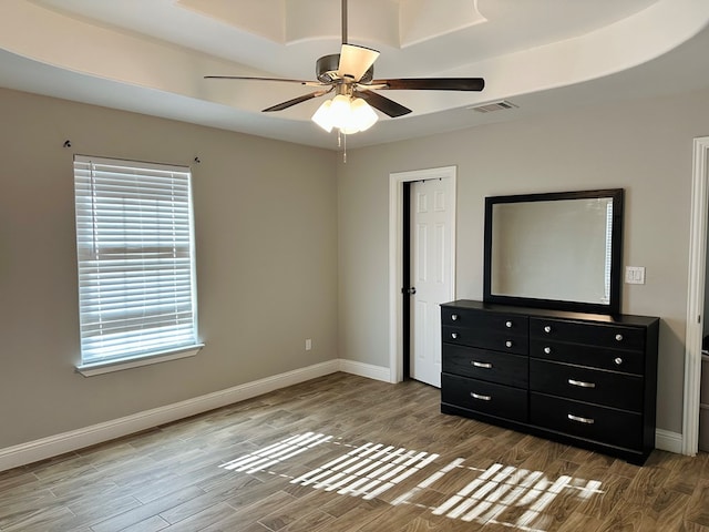 unfurnished bedroom with hardwood / wood-style floors, ceiling fan, and a raised ceiling