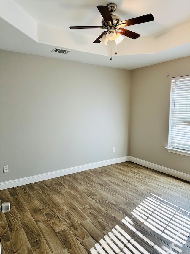 empty room with a tray ceiling, ceiling fan, and hardwood / wood-style flooring