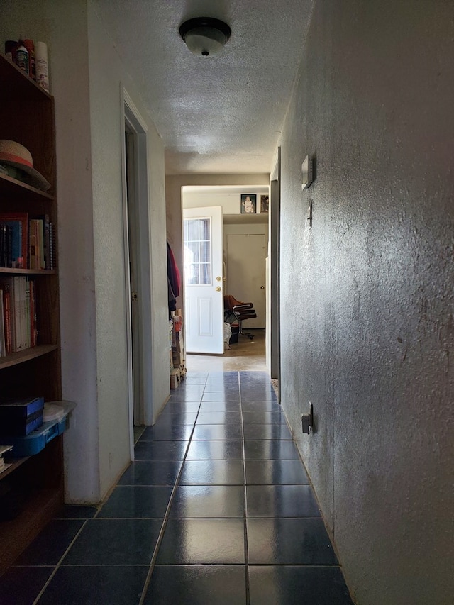 hall with dark tile patterned floors and a textured ceiling