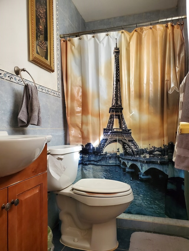 bathroom with walk in shower, vanity, toilet, and tile walls