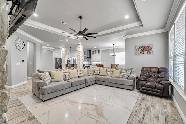 living room featuring crown molding, a tray ceiling, and ceiling fan with notable chandelier