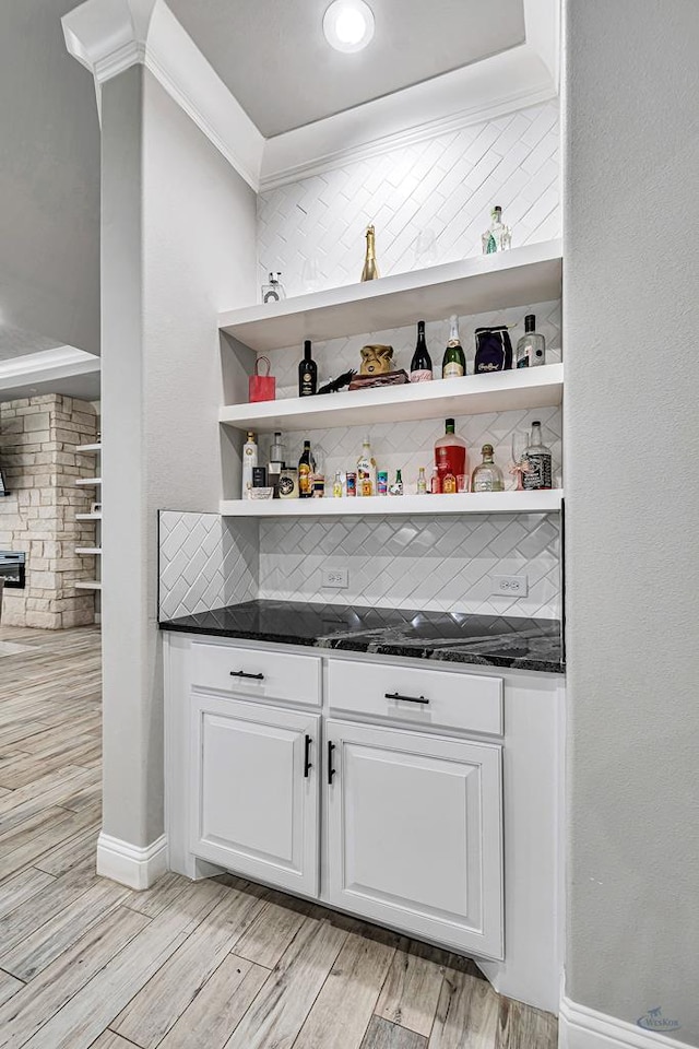 bar featuring dark stone countertops, light wood-type flooring, ornamental molding, white cabinets, and backsplash