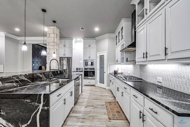 kitchen with wall chimney range hood, dark stone counters, hanging light fixtures, and white cabinets