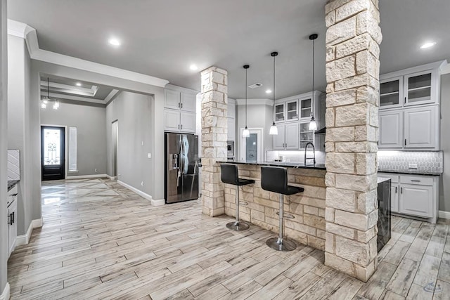 kitchen featuring tasteful backsplash, white cabinets, stainless steel fridge, hanging light fixtures, and crown molding