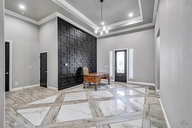 entryway featuring an inviting chandelier, crown molding, a raised ceiling, and a towering ceiling