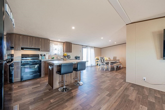 kitchen with dark hardwood / wood-style floors, dark brown cabinetry, ventilation hood, a kitchen island, and black range oven