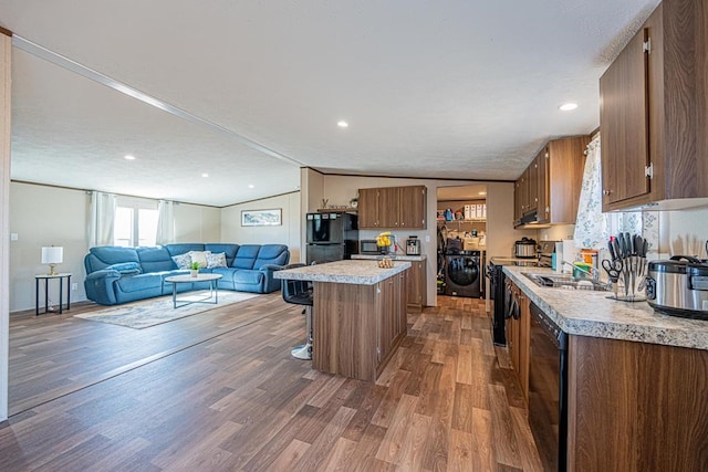 kitchen with dark hardwood / wood-style floors, lofted ceiling, a breakfast bar area, a center island, and independent washer and dryer