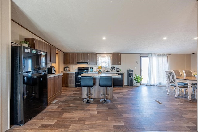 kitchen featuring a breakfast bar, extractor fan, black appliances, a kitchen island, and dark hardwood / wood-style flooring