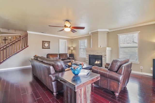 living room featuring ceiling fan, a stone fireplace, crown molding, and dark wood-type flooring