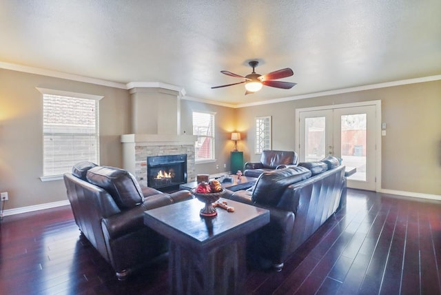 living room with french doors, ornamental molding, ceiling fan, dark hardwood / wood-style floors, and a stone fireplace