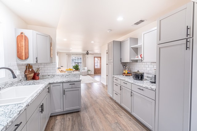 kitchen with light stone counters, sink, light hardwood / wood-style flooring, and gray cabinetry