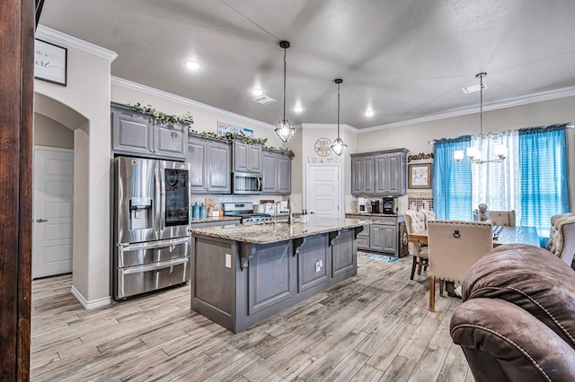 kitchen featuring light stone counters, appliances with stainless steel finishes, a kitchen island with sink, pendant lighting, and light hardwood / wood-style floors