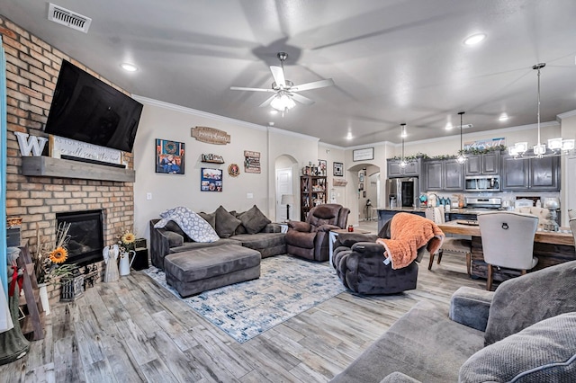 living room with a fireplace, crown molding, light hardwood / wood-style flooring, and ceiling fan