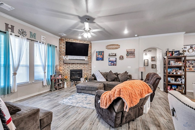 living room with crown molding, a fireplace, ceiling fan, and light wood-type flooring