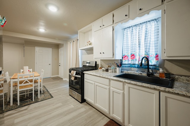 kitchen featuring gas range, white cabinetry, and sink