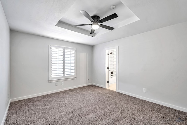 carpeted empty room featuring a raised ceiling and ceiling fan