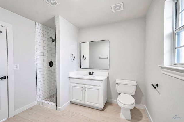 bathroom featuring hardwood / wood-style flooring, vanity, toilet, and tiled shower