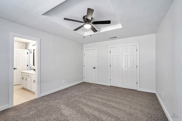 unfurnished bedroom with light carpet, ensuite bathroom, a raised ceiling, and ceiling fan