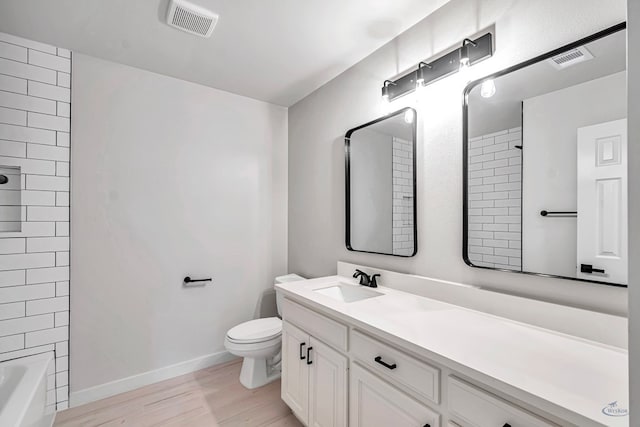 full bathroom featuring hardwood / wood-style flooring, vanity, tiled shower / bath combo, and toilet