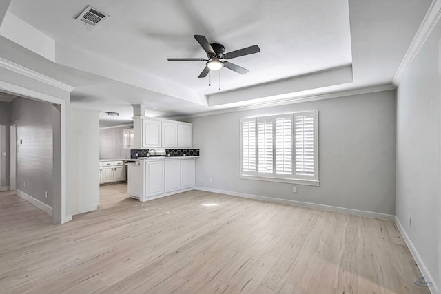 unfurnished living room with a raised ceiling, ceiling fan, light hardwood / wood-style flooring, and ornamental molding