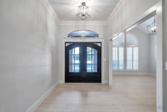 foyer featuring a chandelier, light wood-type flooring, crown molding, and french doors