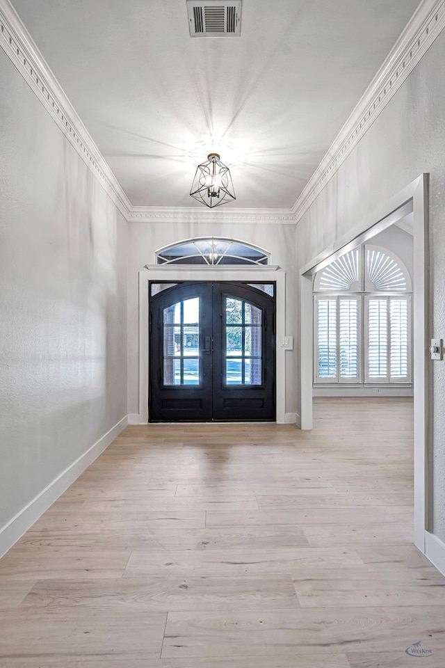 foyer entrance with ornamental molding, french doors, light hardwood / wood-style flooring, and a notable chandelier