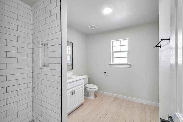 bathroom featuring hardwood / wood-style flooring, vanity, toilet, and tiled shower