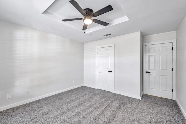 unfurnished bedroom with carpet flooring, a closet, a tray ceiling, and ceiling fan