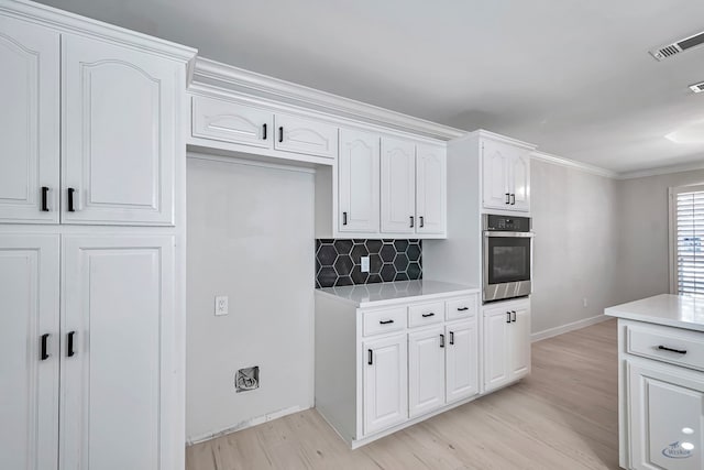 kitchen with light wood-type flooring, backsplash, ornamental molding, white cabinets, and oven