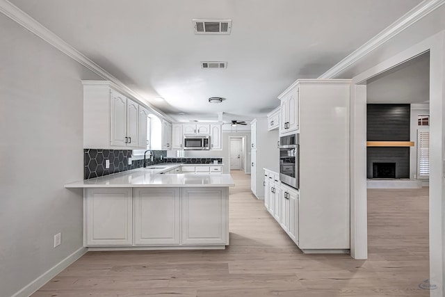 kitchen with kitchen peninsula, appliances with stainless steel finishes, tasteful backsplash, sink, and white cabinetry