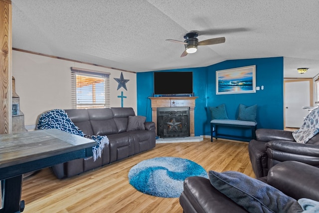 living room with a textured ceiling, lofted ceiling, wood finished floors, and a fireplace with raised hearth